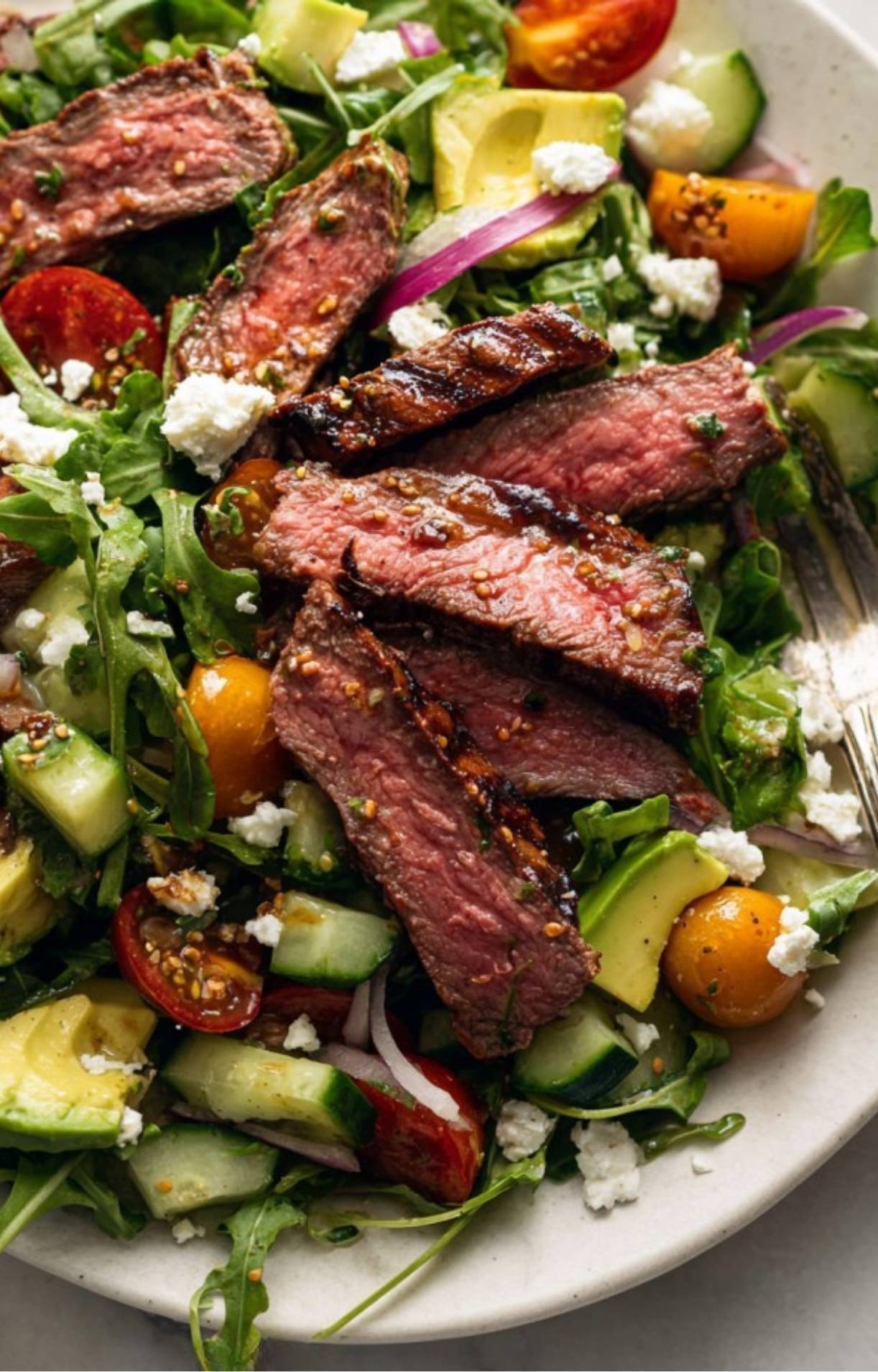 A detailed shot of juicy steak slices combined with crisp cucumbers, tomatoes, and avocado in a steak salad dressing recipe.