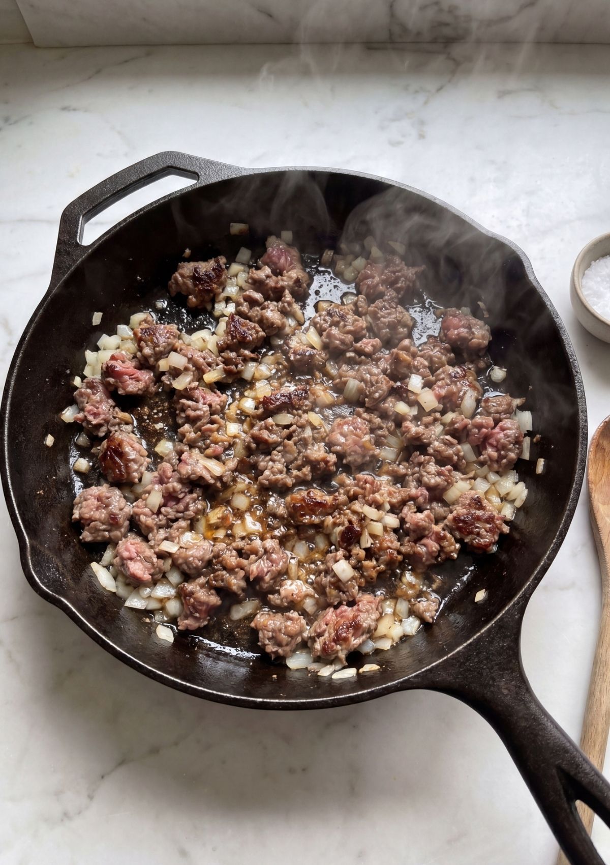 wagyu ground beef cooking with onions in cast iron skillet for slider recipe