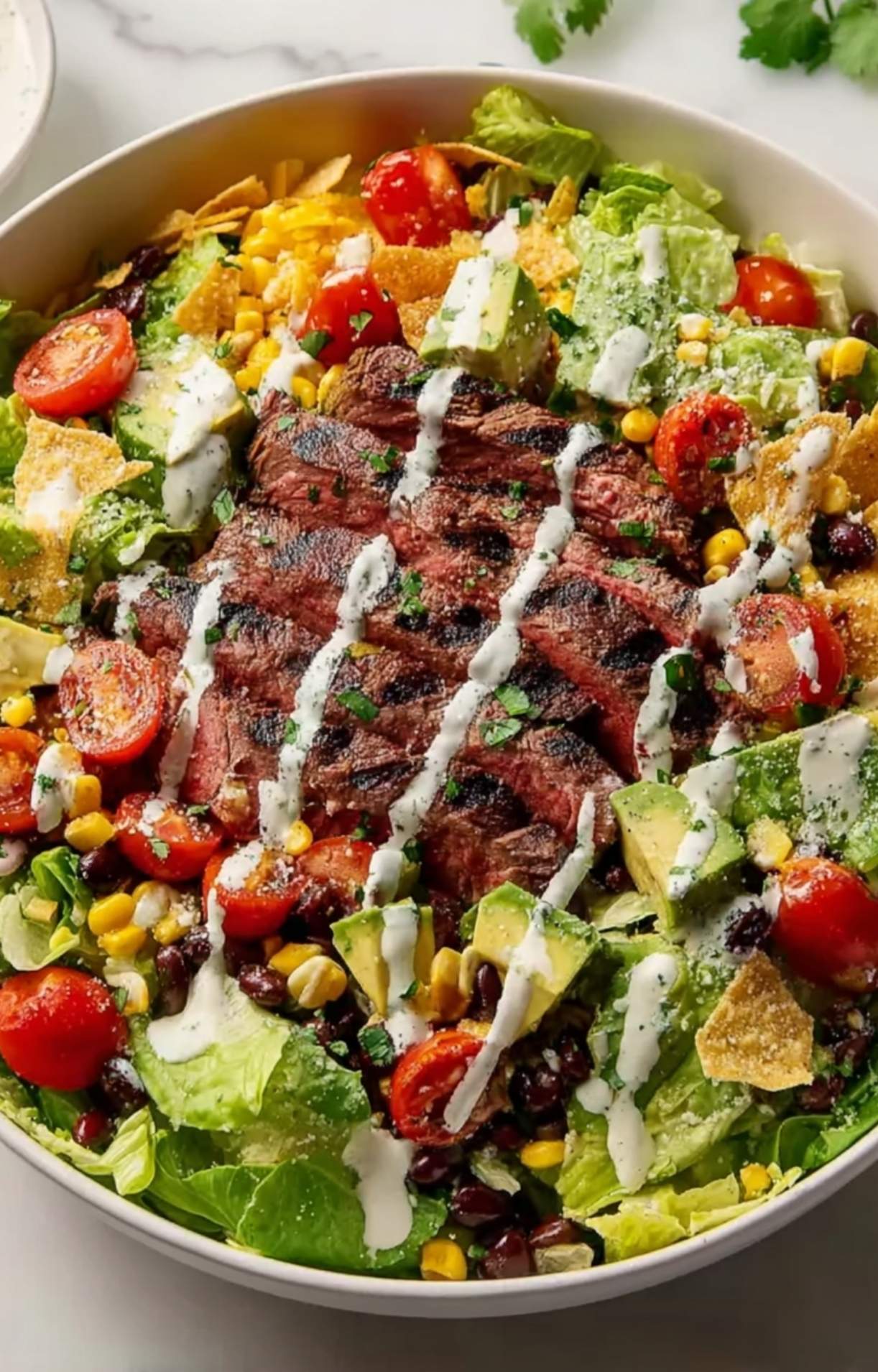 A completed Easy Steak Taco Salad Recipe drizzled with creamy white dressing and garnished with crunchy tortilla chips and fresh cilantro.
