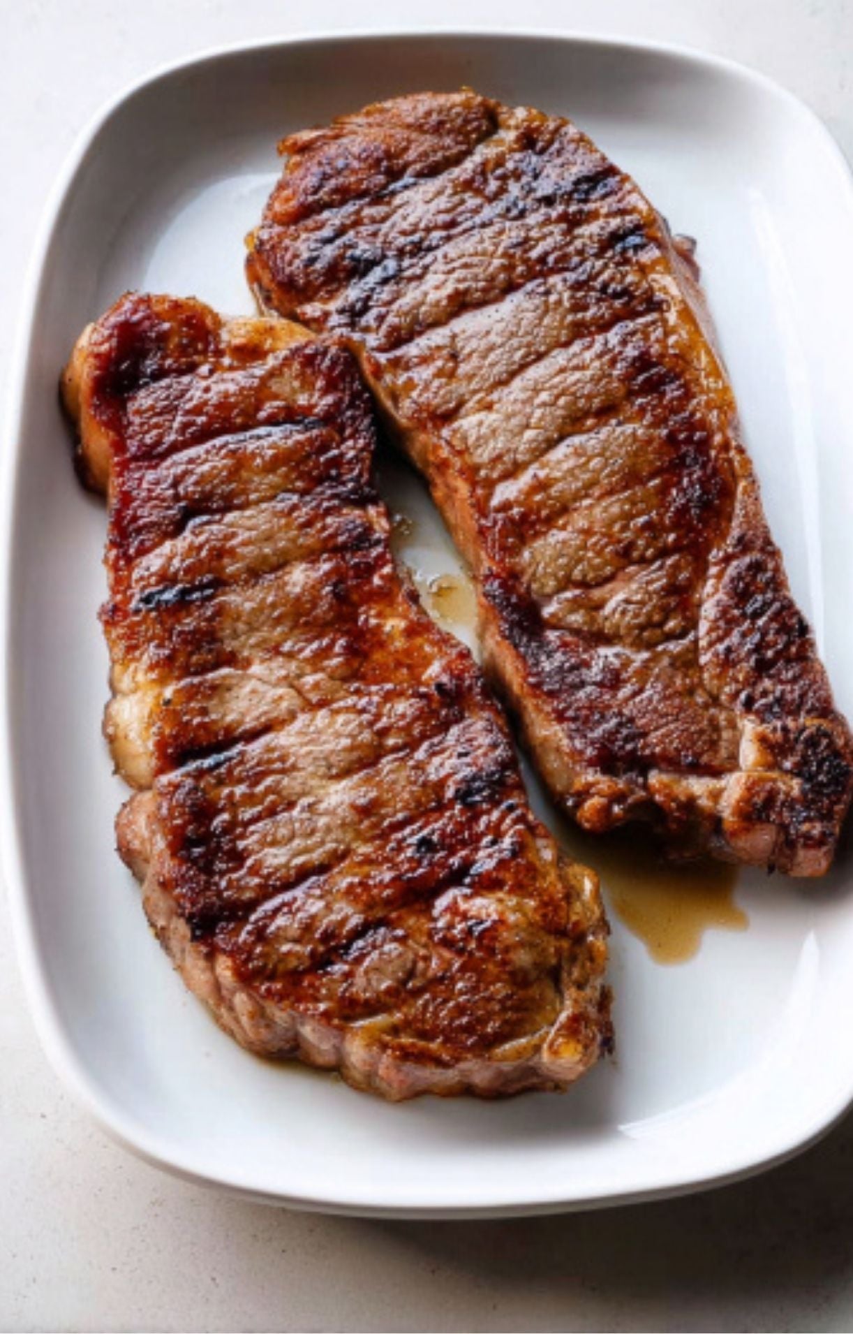 Two golden-brown seared steaks resting on a white platter, showing a caramelized crust and savory juices.