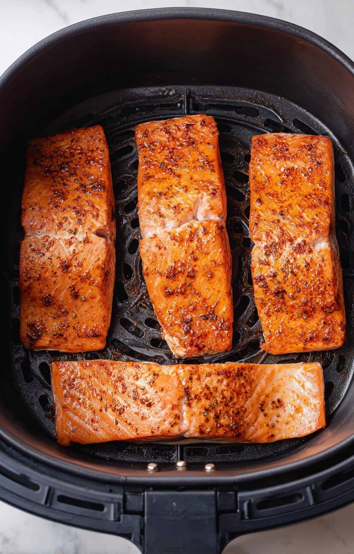 Four seasoned salmon fillets placed inside a black air fryer basket, ready to cook for an easy air fryer salmon recipe.