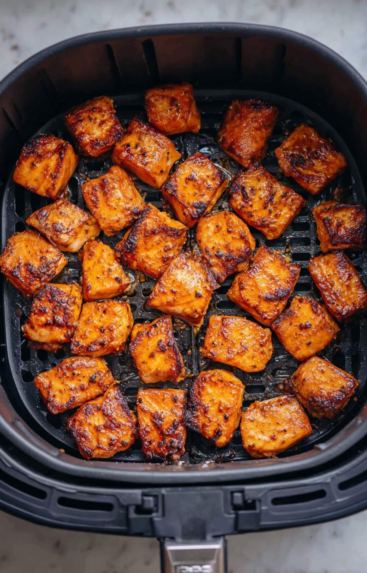 The finished Air Fryer Salmon Bites inside the air fryer basket, showing a dark, caramelized crust and juicy interior after cooking.
