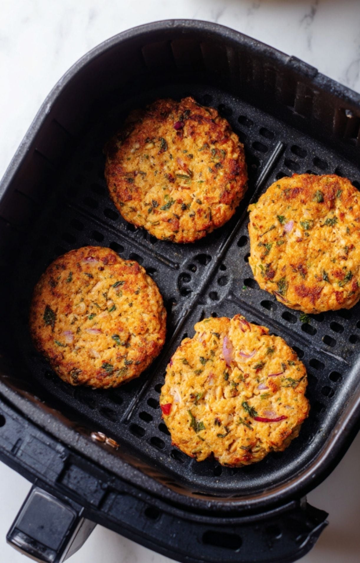 Four salmon patties browning inside a black air fryer basket during the cooking process.