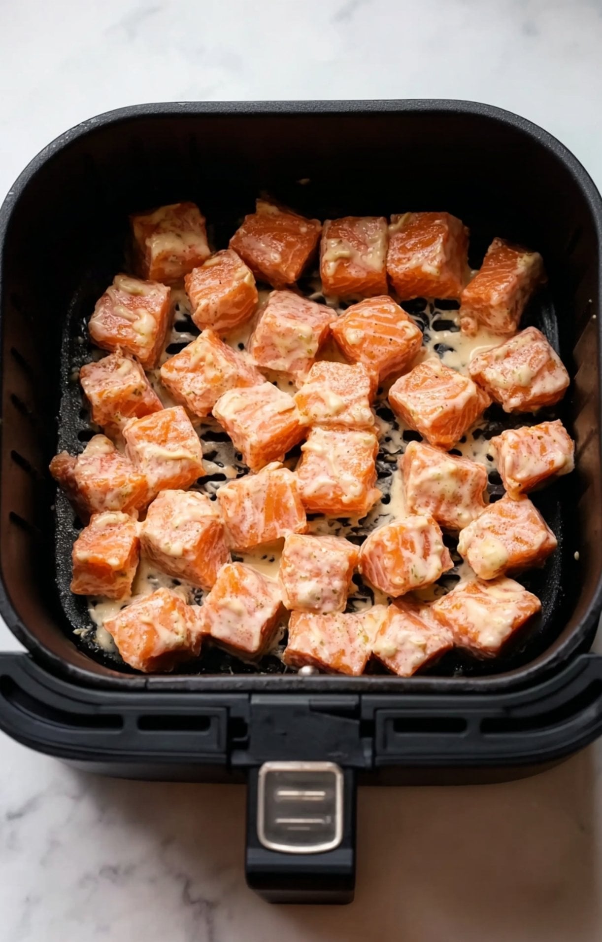 Evenly spaced, marinated salmon cubes arranged in a black air fryer basket ready to be cooked.