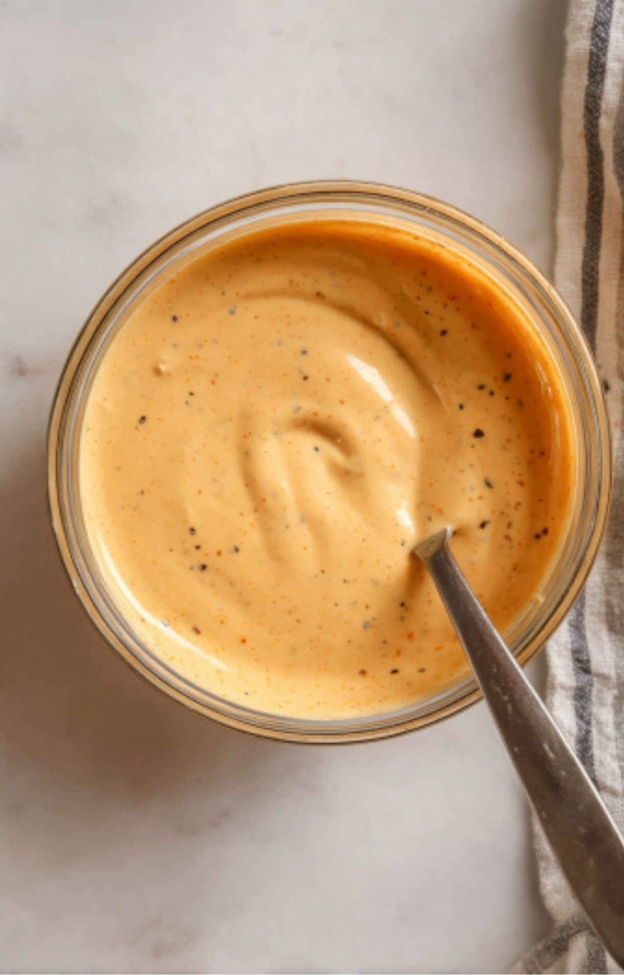 A smooth, orange-tinted creamy dressing in a glass bowl with a spoon, prepared for a Flank Steak Salad Recipe.