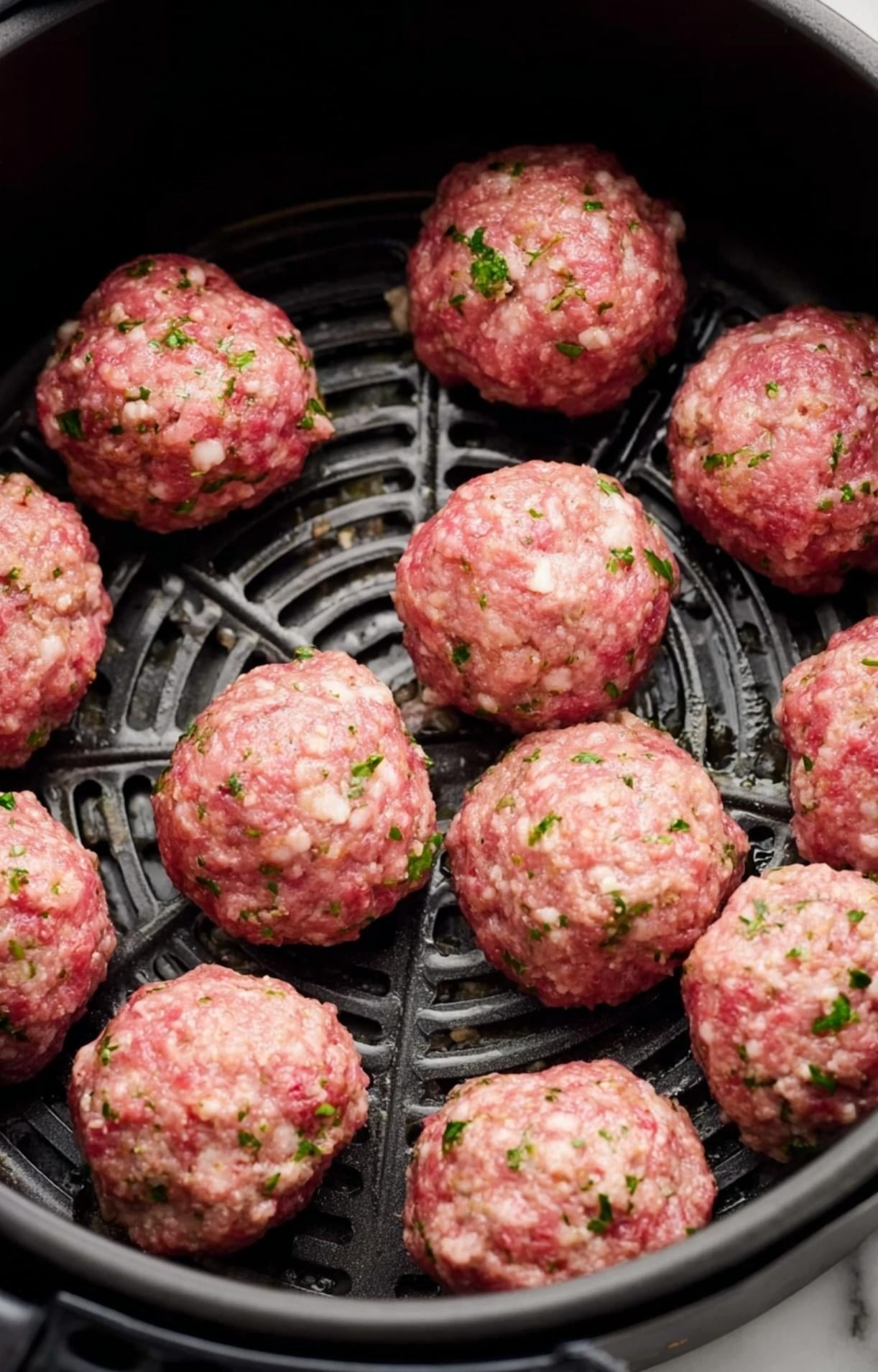 Raw meatballs arranged in a single layer inside a black air fryer basket for optimal airflow.