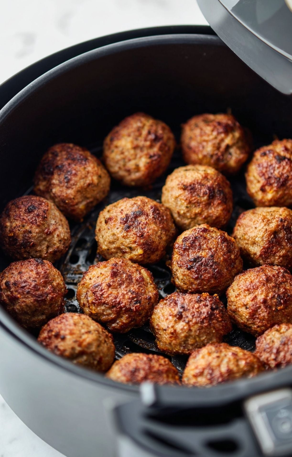 An open air fryer basket filled with a single layer of meatballs browning evenly during the frozen meatballs air fryer process.