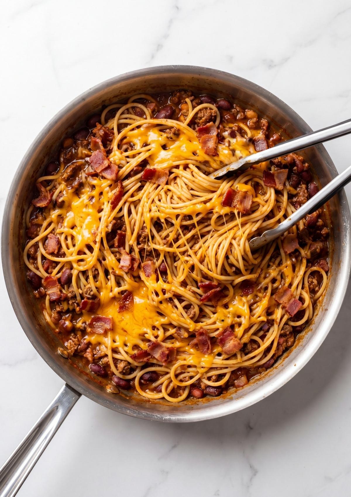 Cowboy spaghetti with bacon in skillet with melted cheddar cheese and crispy bacon easy comfort food dinner