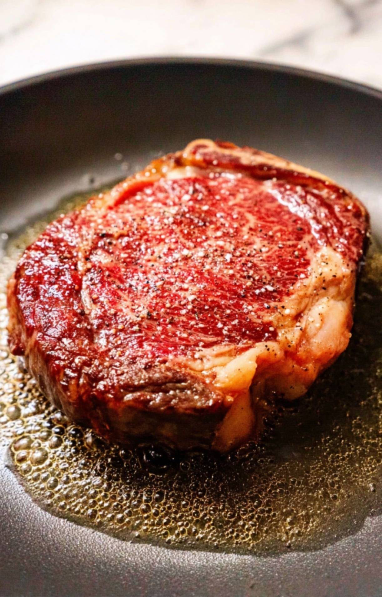 A thick cut of beef searing in a hot pan with bubbling oil to create a golden-brown crust for a Steak Salad Recipe.