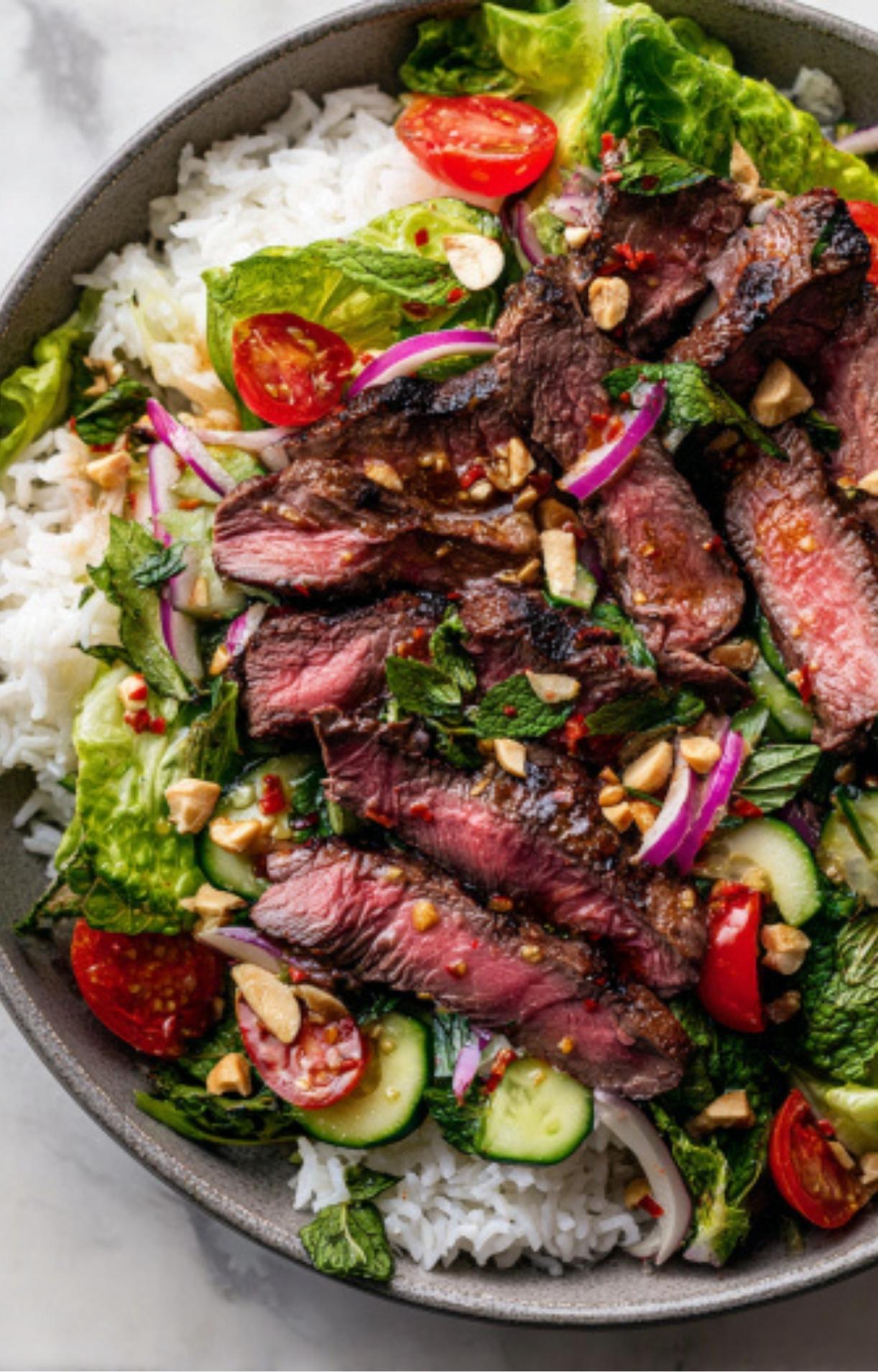 A top-down view of sliced medium-rare steak layered over white rice, fresh greens, and vibrant vegetables in a grey bowl.