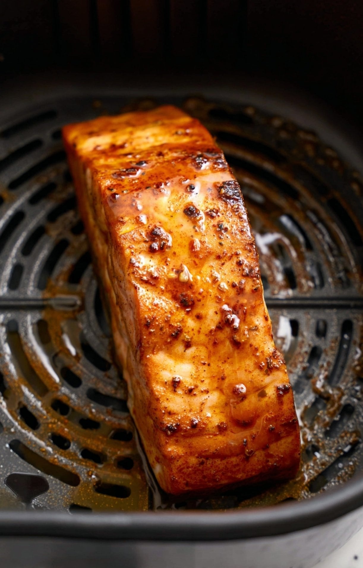A salmon fillet inside an air fryer basket, partially cooked with the marinade beginning to caramelize on the surface.