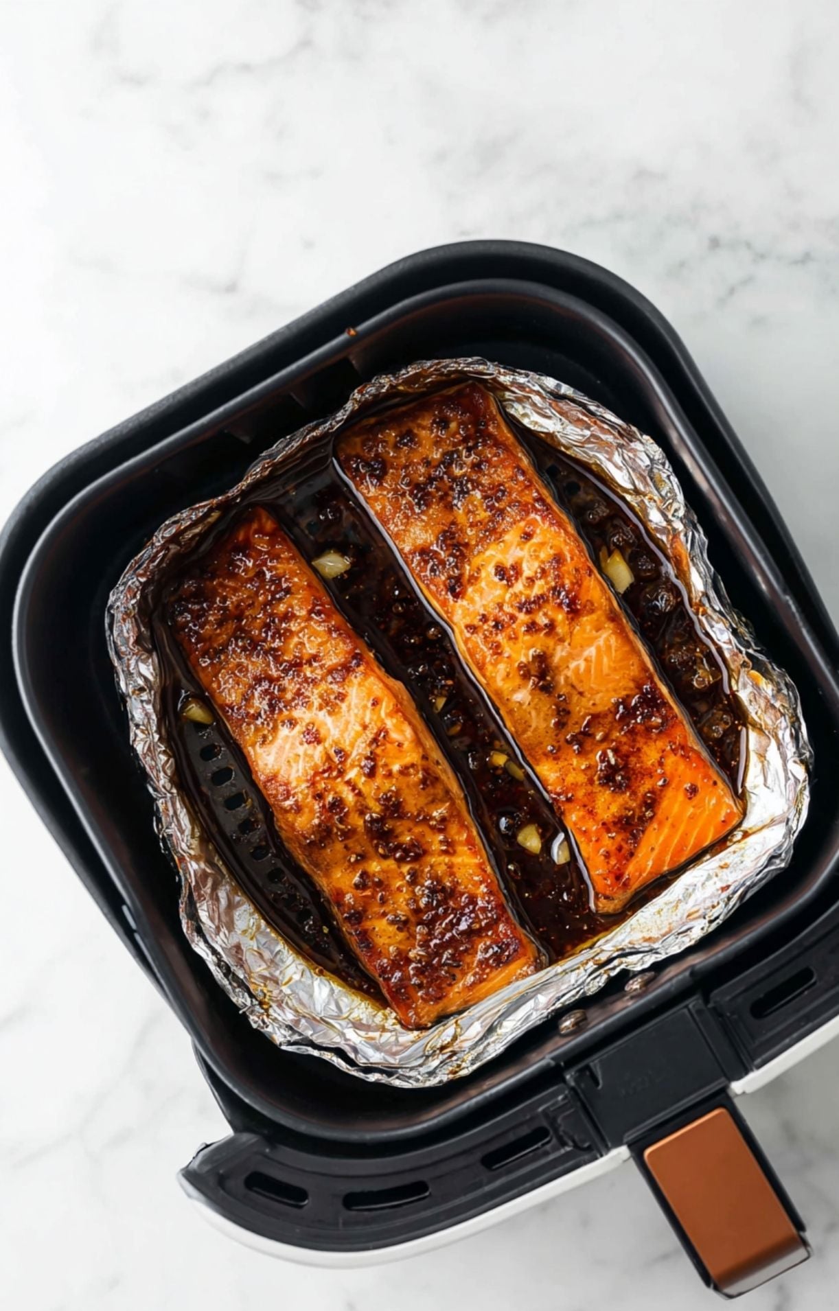 Cooked honey garlic salmon fillets in the air fryer basket showing a beautiful caramelized glaze and charred edges.