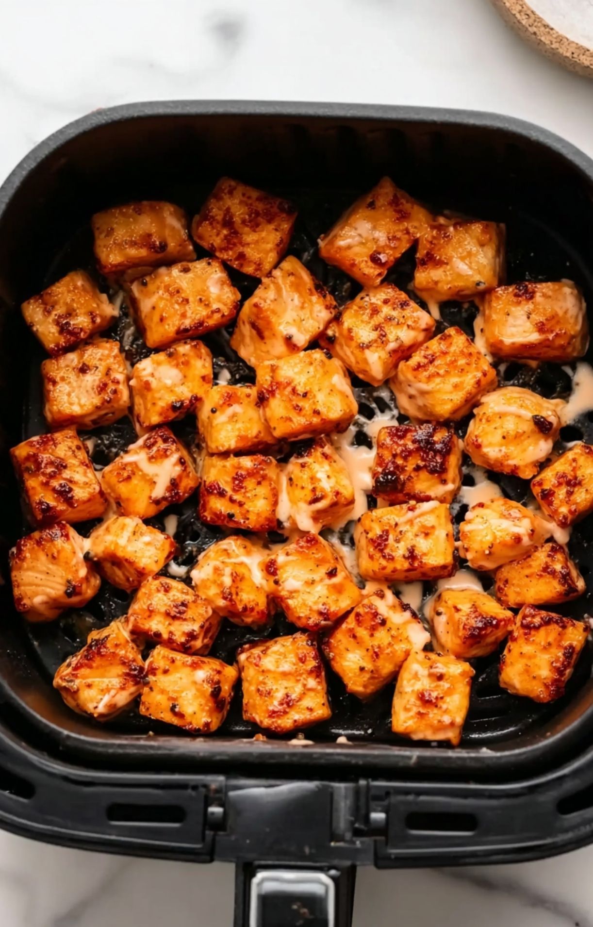 Golden-brown, crispy air-fried salmon cubes sitting in an air fryer basket after the cooking process.