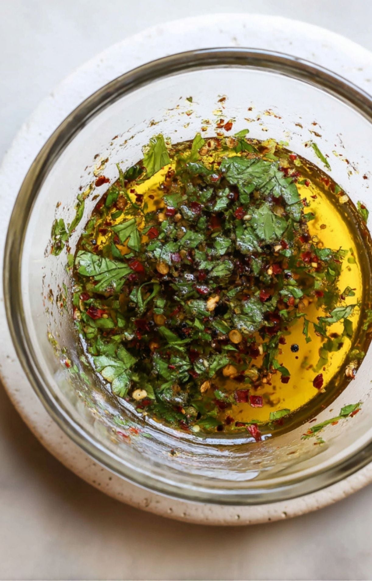 A glass bowl containing olive oil, red pepper flakes, and freshly chopped herbs for a Flank Steak Salad Recipe.
