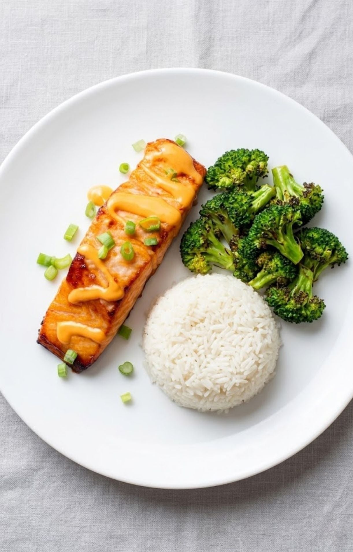 A white plate featuring a salmon fillet, a scoop of white rice, and broccoli.