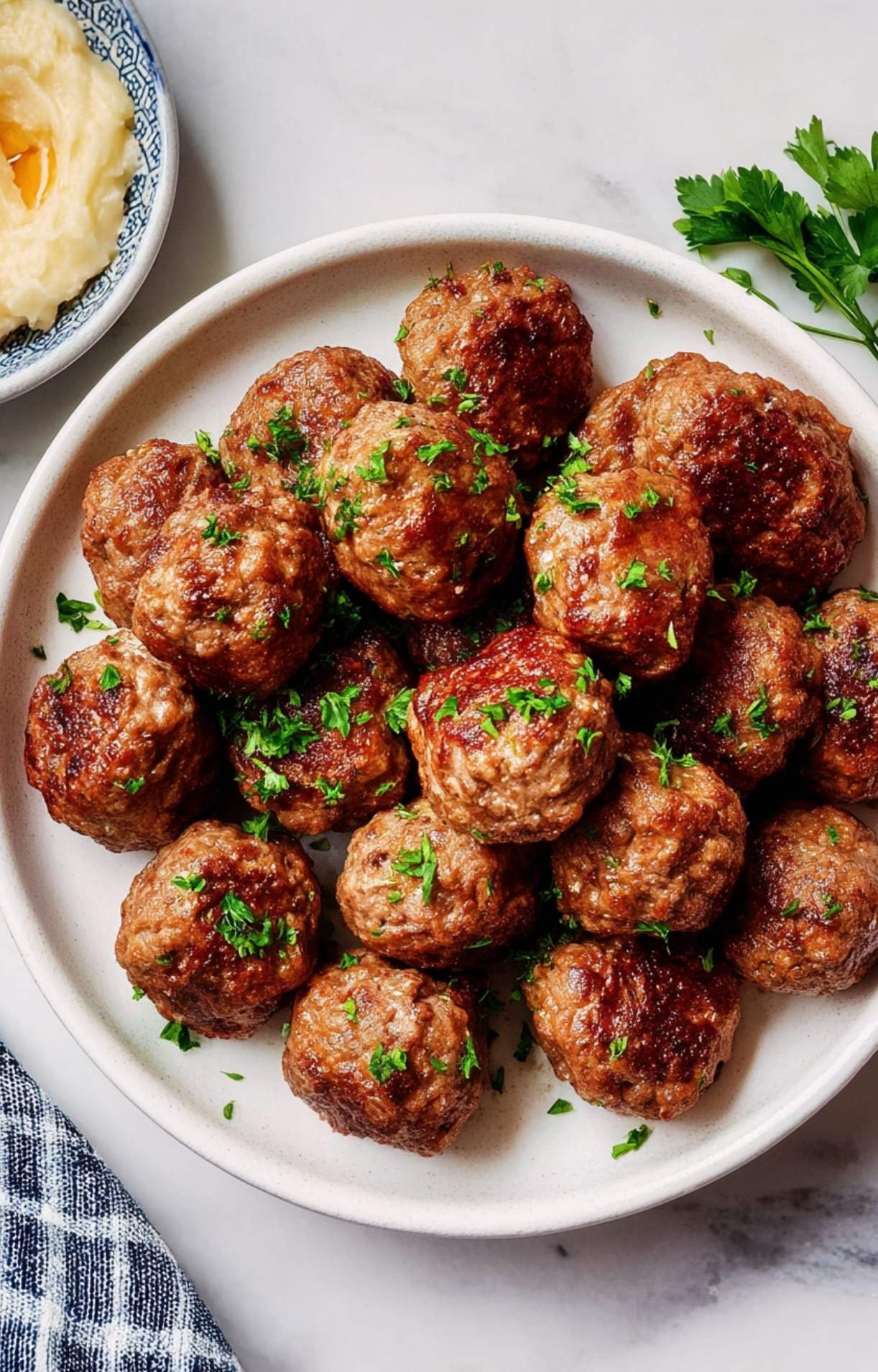 A white ceramic plate piled high with seasoned meatballs next to a side of creamy potatoes.