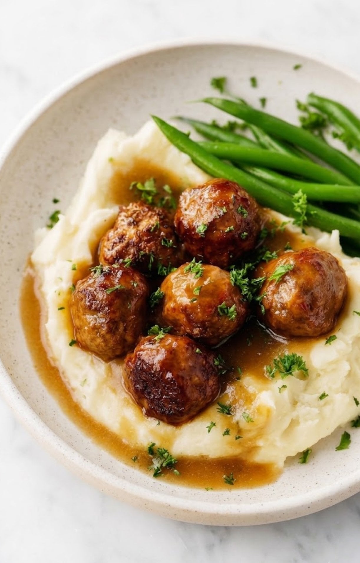 A beautifully plated meal featuring glazed chicken meatballs, mashed potatoes, and fresh green beans.