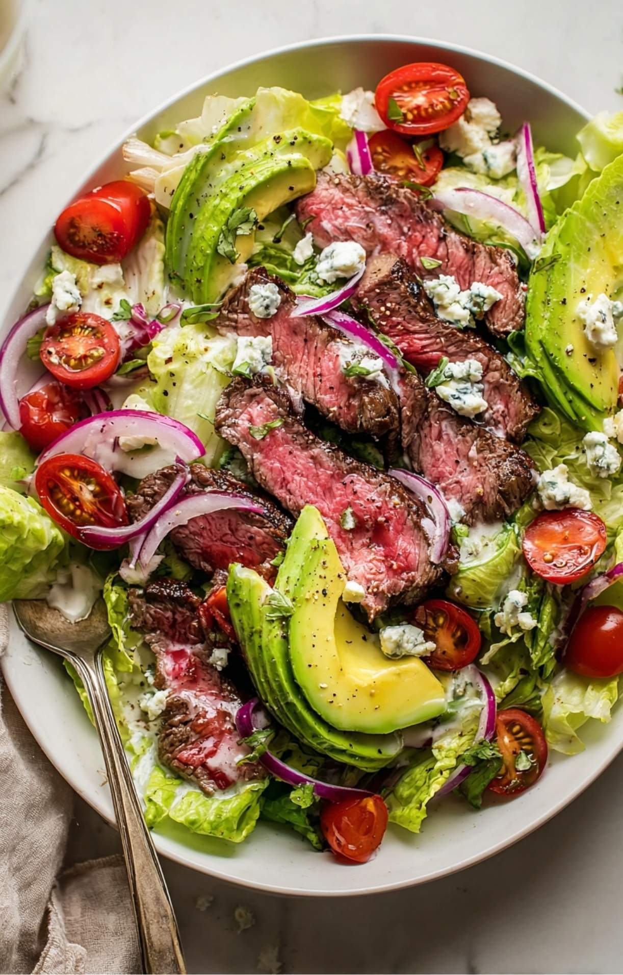A top-down view of a completed Steak and Blue Cheese Salad, showcasing the contrast of charred beef and fresh, crisp garden vegetables.