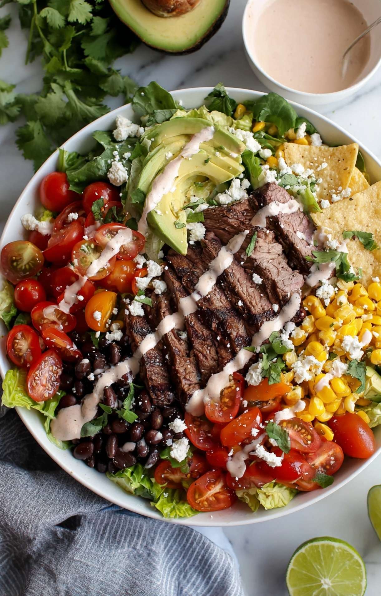 A beautifully presented Easy Steak Taco Salad Recipe bowl served with lime wedges, cilantro, and tortilla chips on a marble surface.