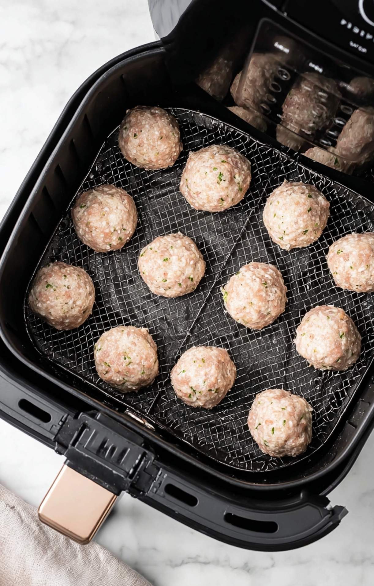 Raw chicken meatballs evenly spaced on a wire rack inside an air fryer ready to be cooked.