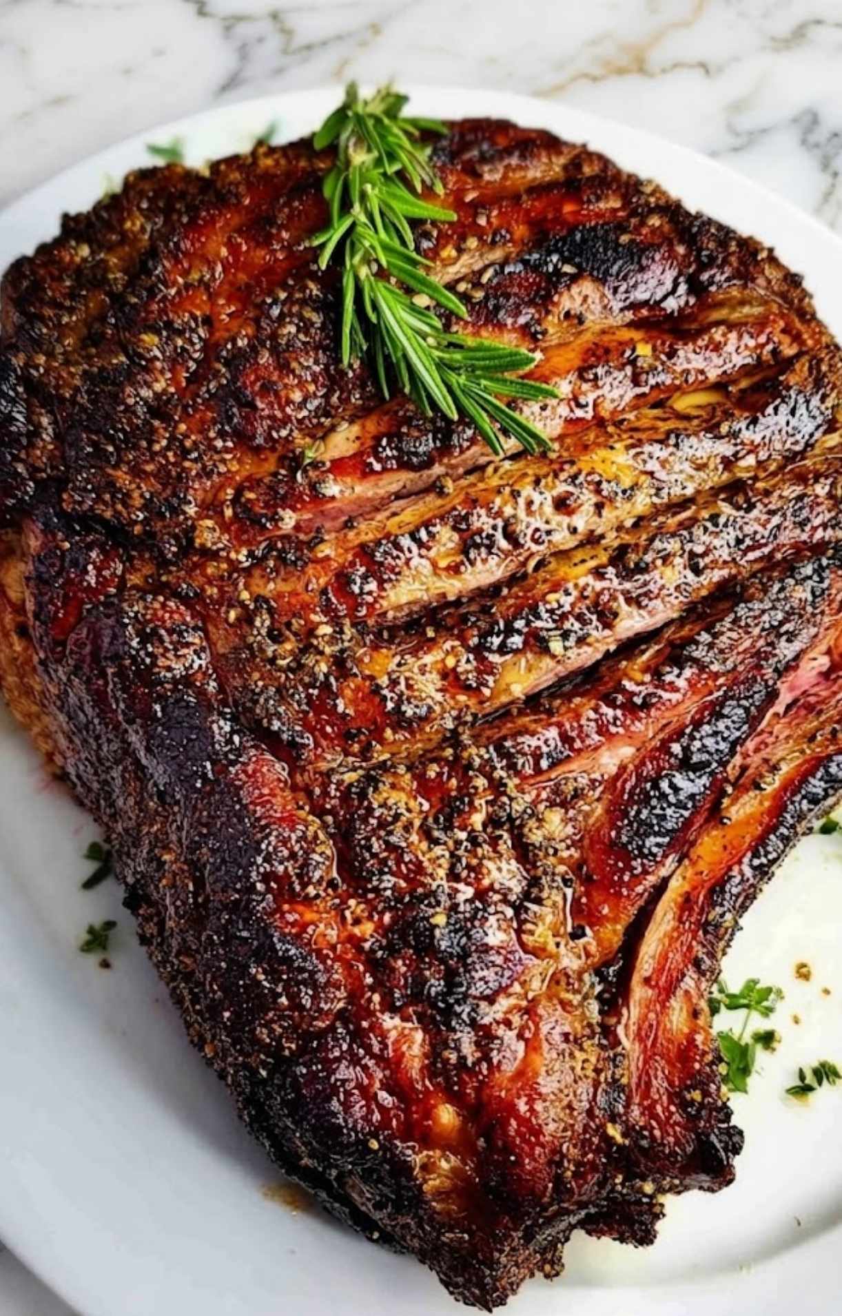 A top-down view of the entire smoked prime rib roast on a white plate, showing the beautifully charred crust and fresh rosemary garnish.