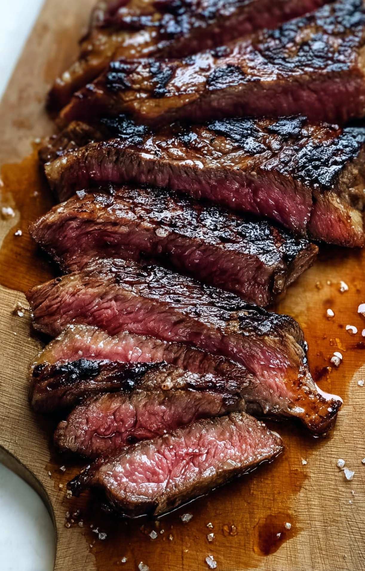 Perfectly cooked steak sliced into thick strips on a wooden cutting board, showing a pink medium-rare center and resting juices.