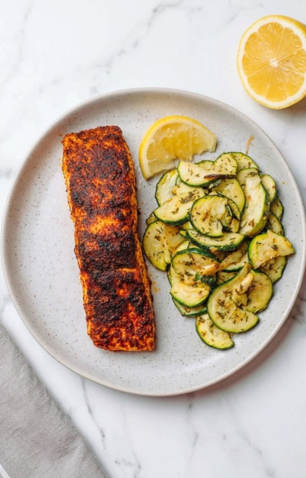 A top-down view of a plated air fryer salmon fillet served with sautéed zucchini rounds and a lemon wedge.