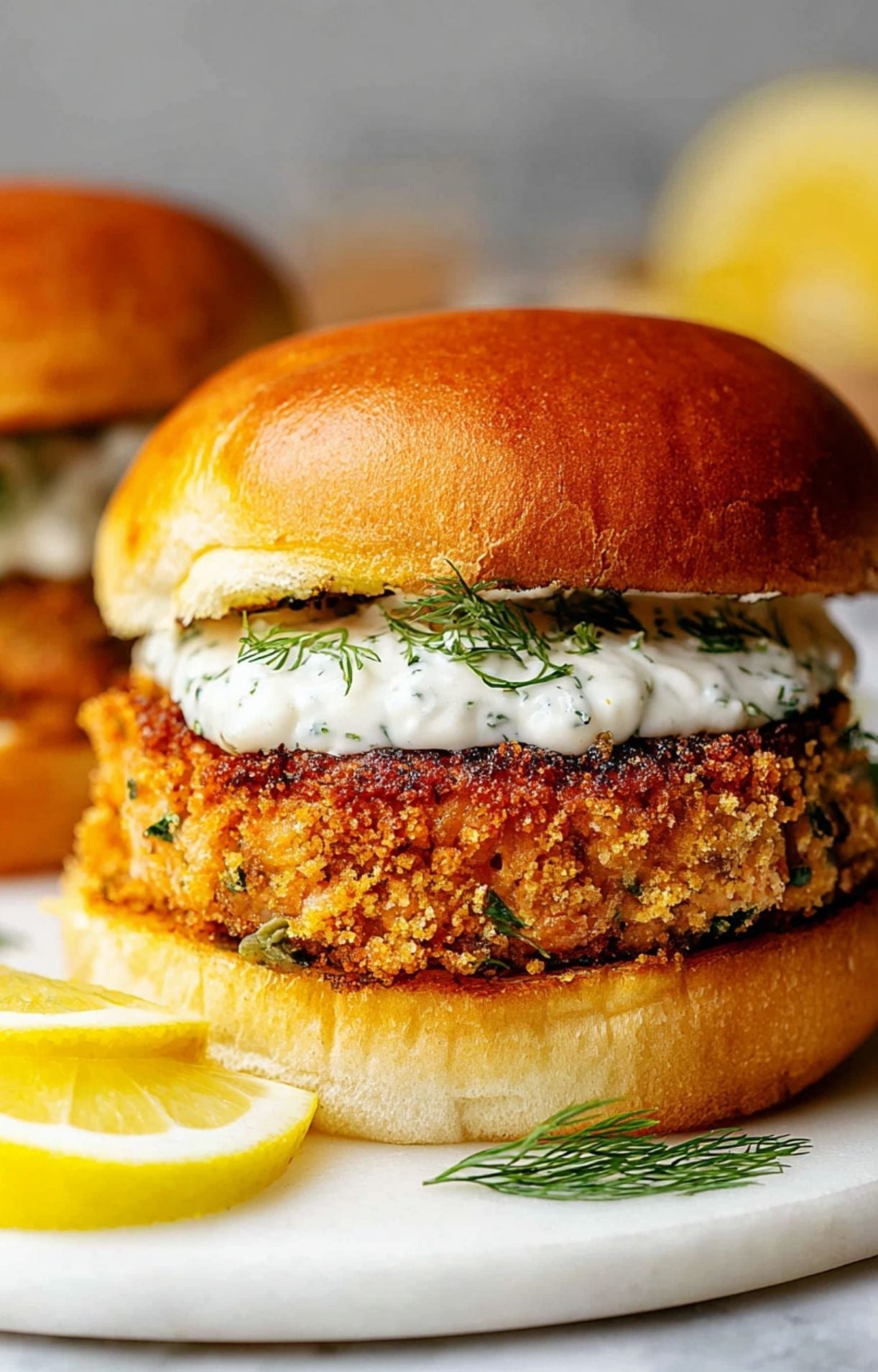 A macro shot showing the layers of a crispy salmon patty, creamy sauce, and fresh dill on a toasted bun.
