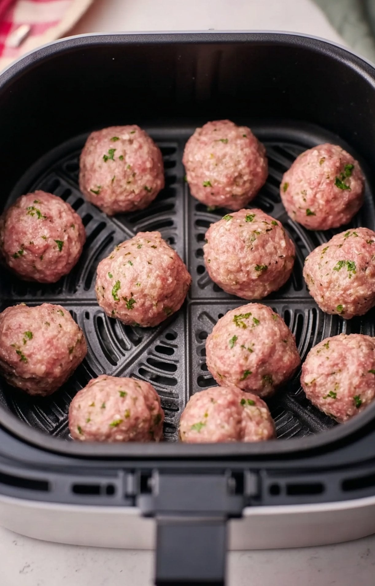 Twelve raw meatballs spaced evenly in a black air fryer basket ready to be cooked.