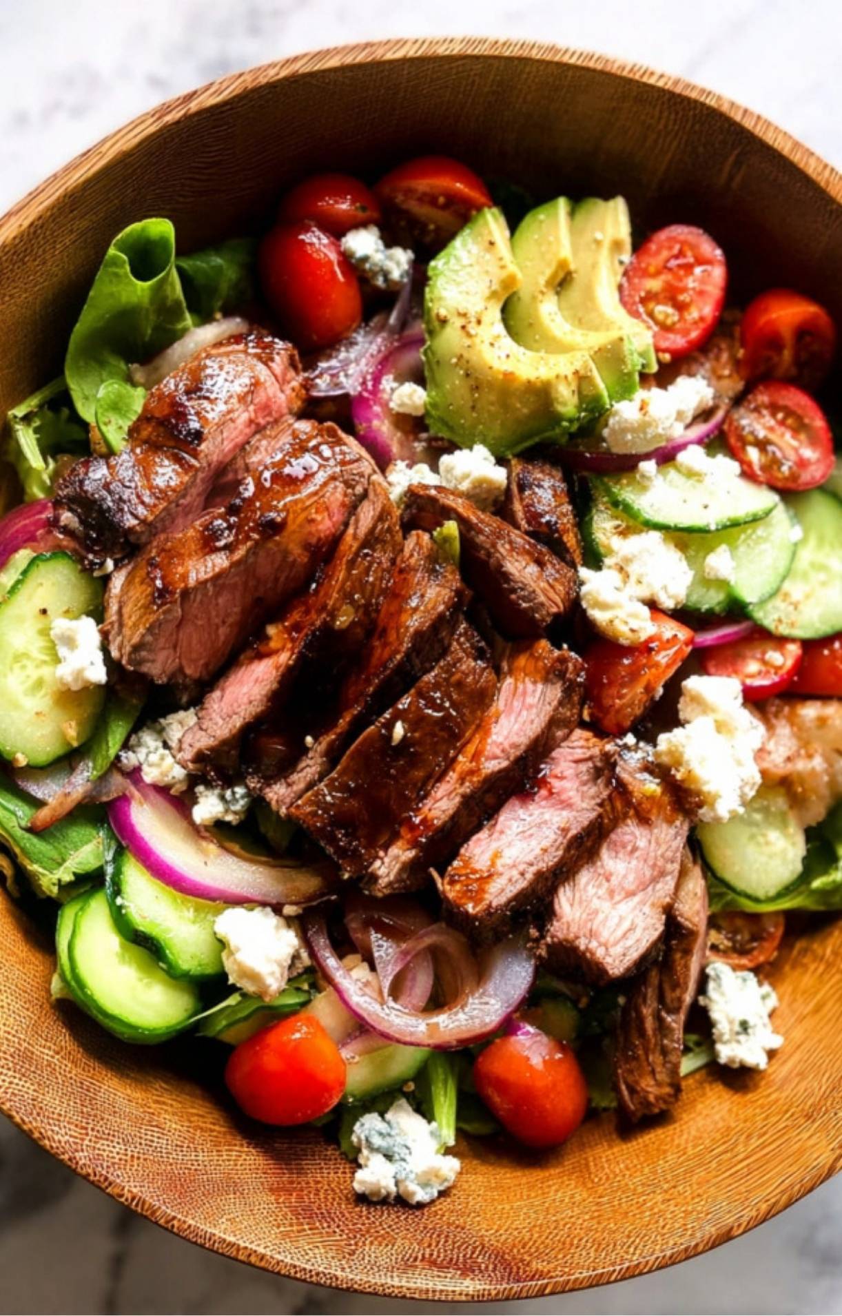 The completed Steak Salad Recipe topped with a drizzle of balsamic glaze and generous crumbles of blue cheese in a wooden serving bowl.