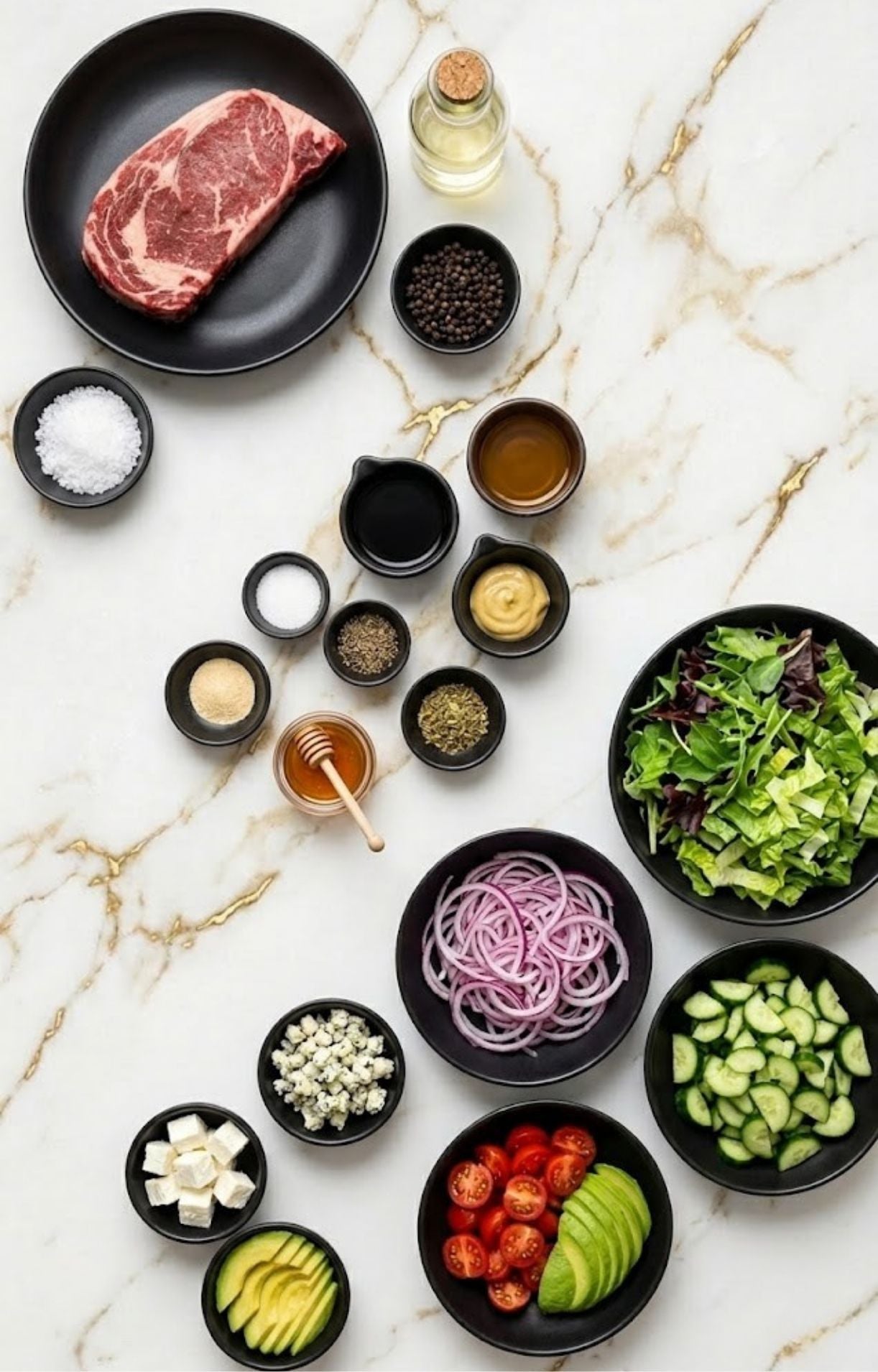 A flat-lay arrangement of Steak Salad Recipe ingredients on a marble surface, including raw ribeye steak, fresh greens, red onions, cucumbers, cherry tomatoes, avocado, blue cheese, and various dressing spices.