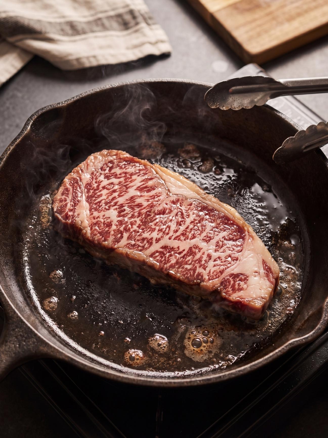 wagyu beef marbling recipe step showing steak cooking in skillet with tongs and melted fat