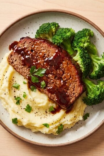 A fork holding a bite sized piece of glazed meatloaf topped with a dollop of mashed potatoes