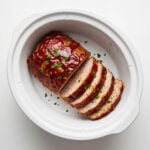 Slices of glazed turkey meatloaf fanned out inside a white slow cooker insert against a clean white background