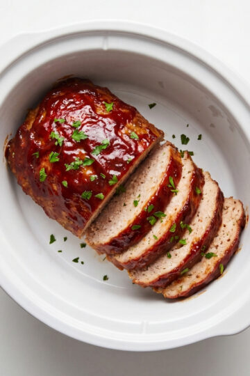Slices of glazed turkey meatloaf fanned out inside a white slow cooker insert against a clean white background