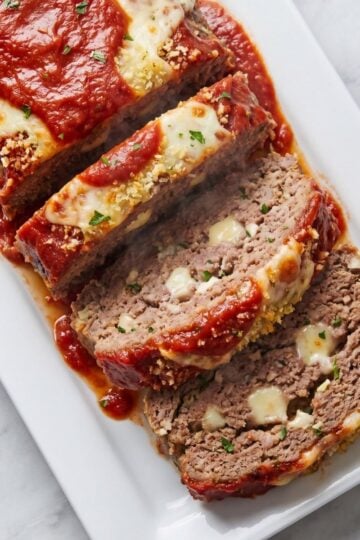 Several thick slices of Italian meatloaf arranged on a rectangular plate, showing a cheesy center and rich tomato glaze.
