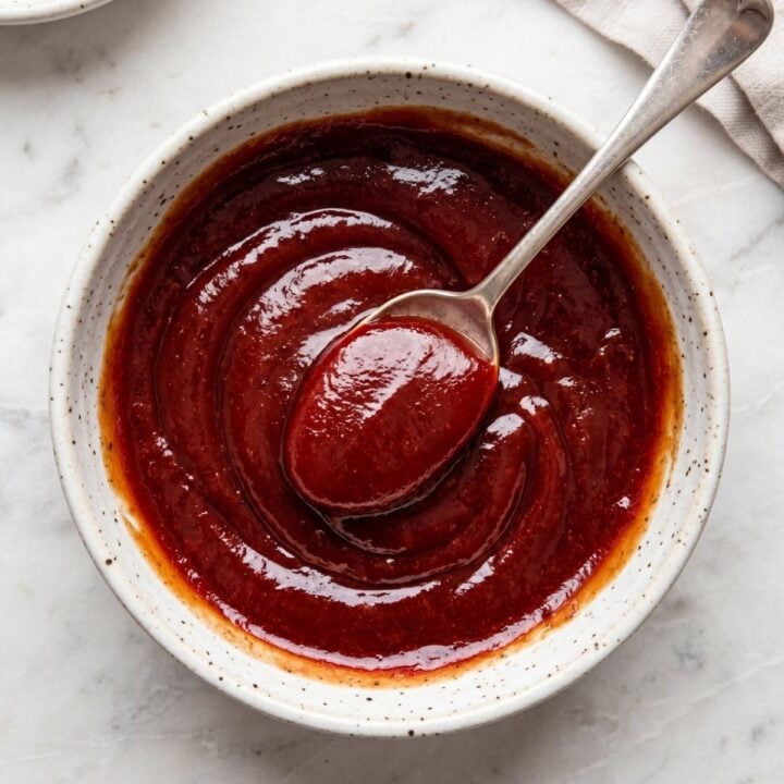 A top-down close-up of a thick, red Meatloaf Glaze Recipe with a spoon resting in the center of the bowl.