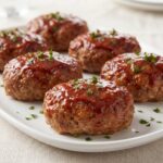 Six mini turkey meatloaves with a glossy red glaze arranged on a white serving platter and garnished with fresh chopped parsley