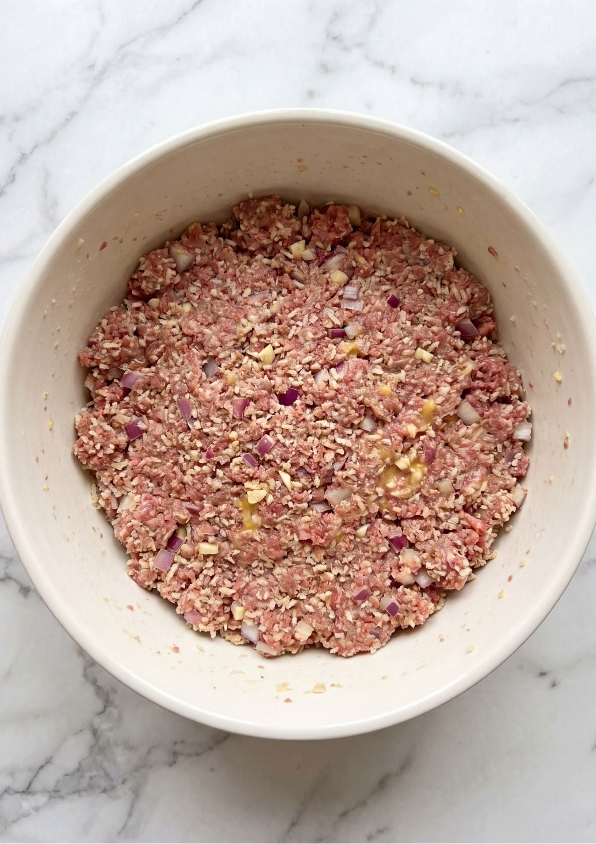 A white bowl filled with a well-combined mixture of ground beef, onions, and spices, ready to be shaped for the smoker.