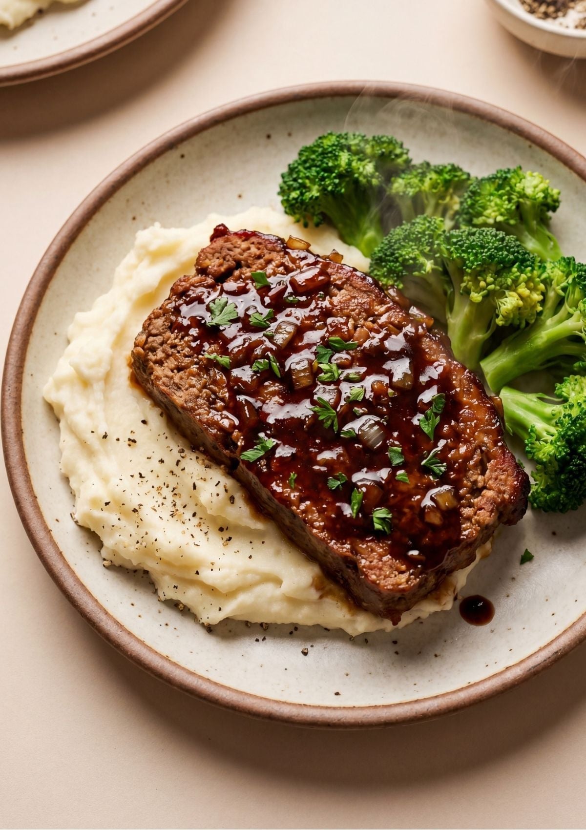 A plate featuring a thick slice of glazed meatloaf served with creamy mashed potatoes and fresh green broccoli