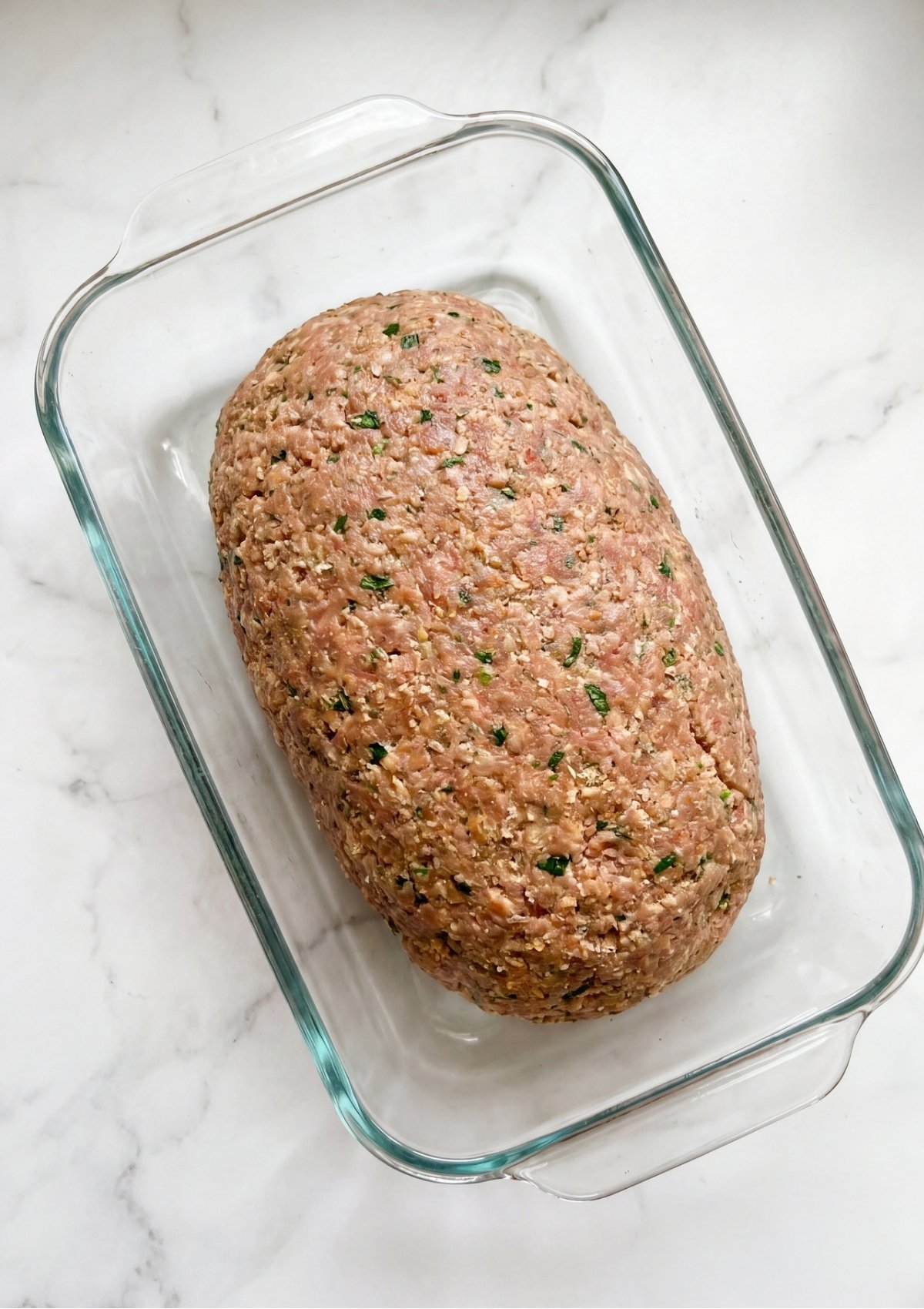 Raw ground beef mixture shaped into a neat loaf inside a clear glass rectangular baking dish