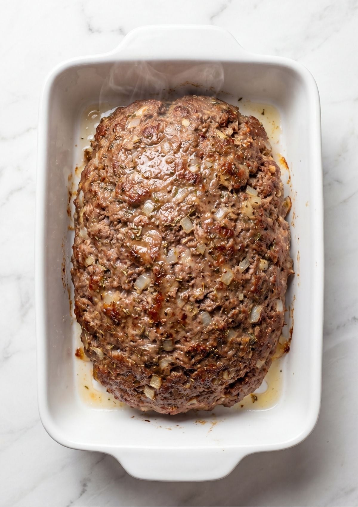Fully cooked plain meatloaf in a white baking dish showing rendered juices and a browned exterior.