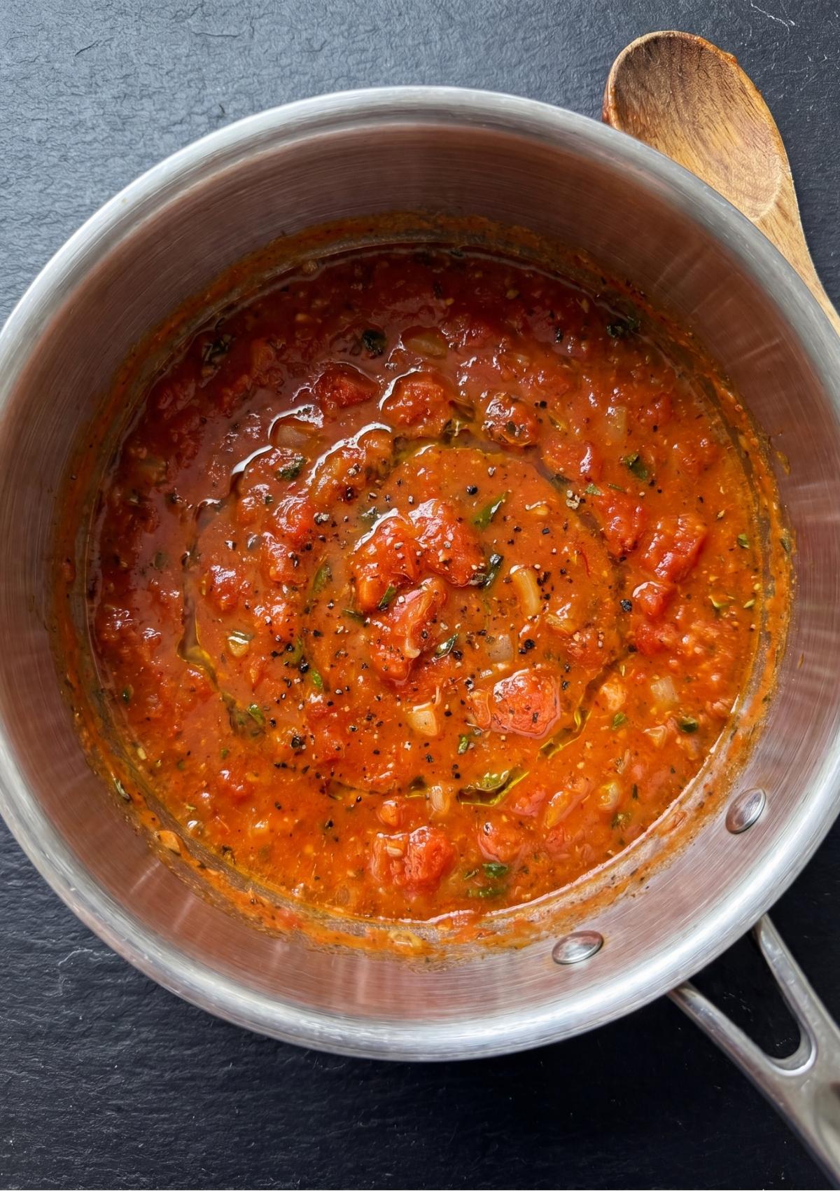 Sautéed chopped onions, tomato paste, Worcestershire sauce, and herbs simmering in a stainless steel saucepan with a wooden spoon resting nearby.