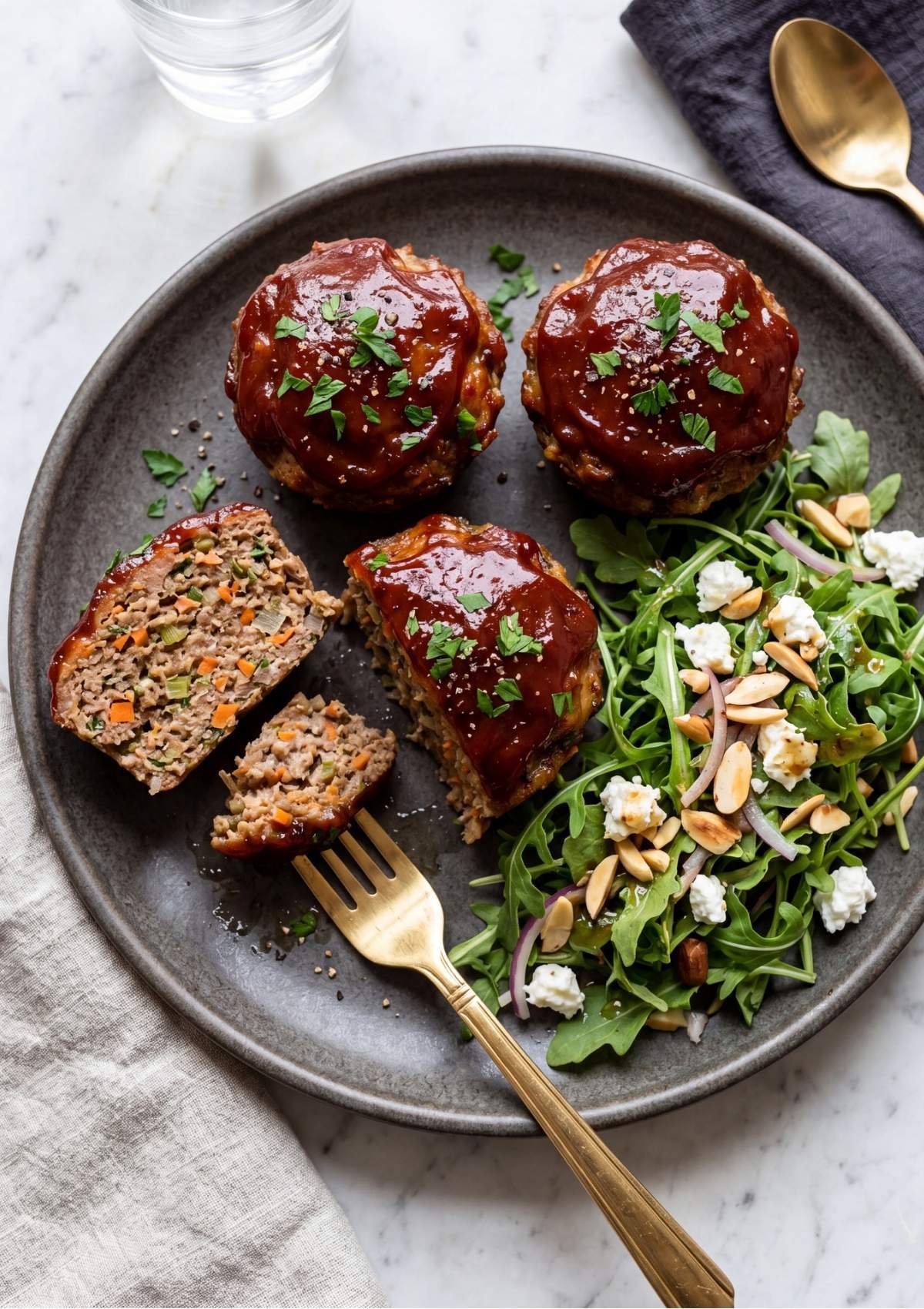 Three glazed mini meatloaves on a plate with an arugula, almond, and feta salad.