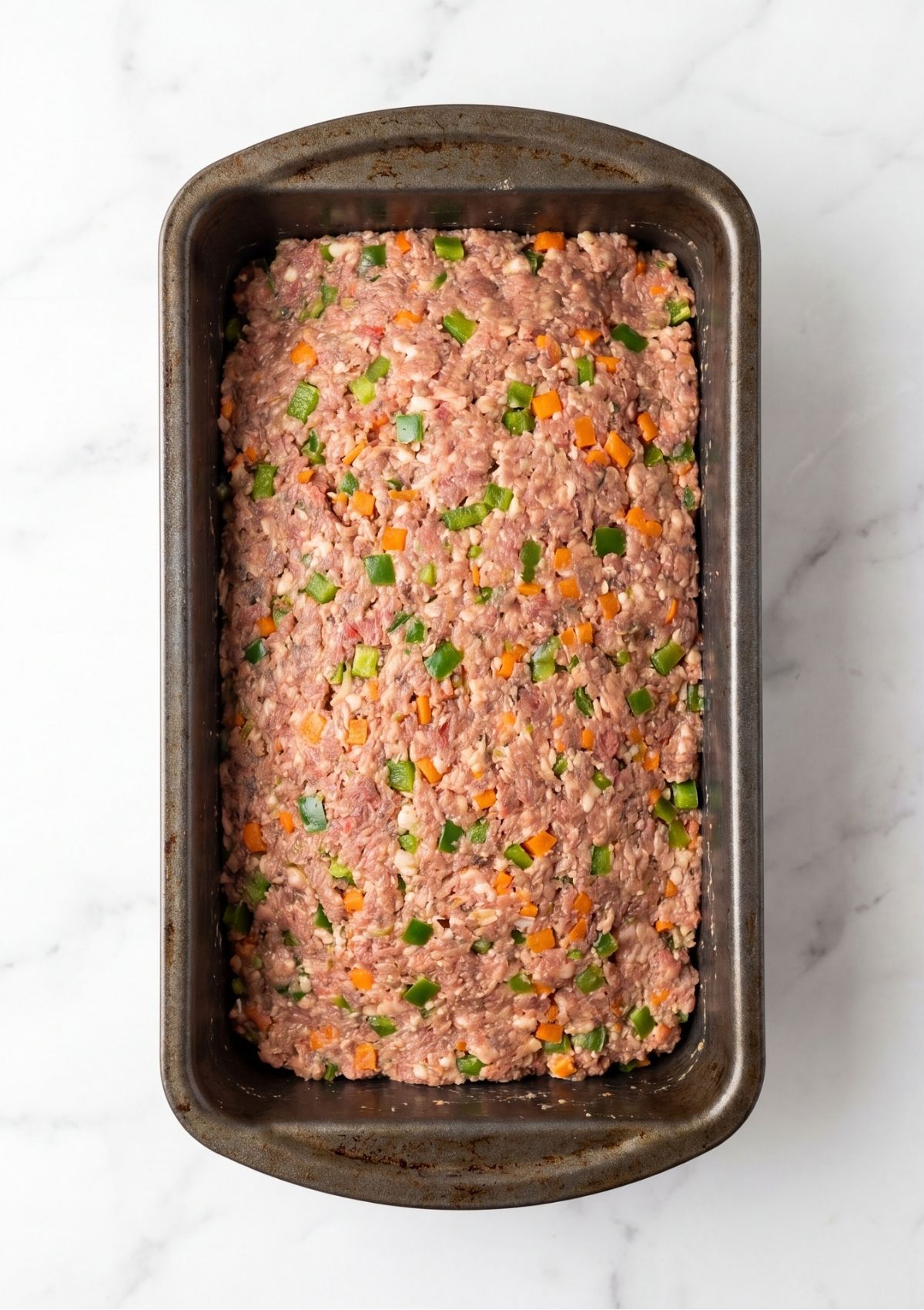 Raw ground turkey and beef meatloaf mixture with visible bits of green bell pepper and carrot pressed into a metal loaf pan.