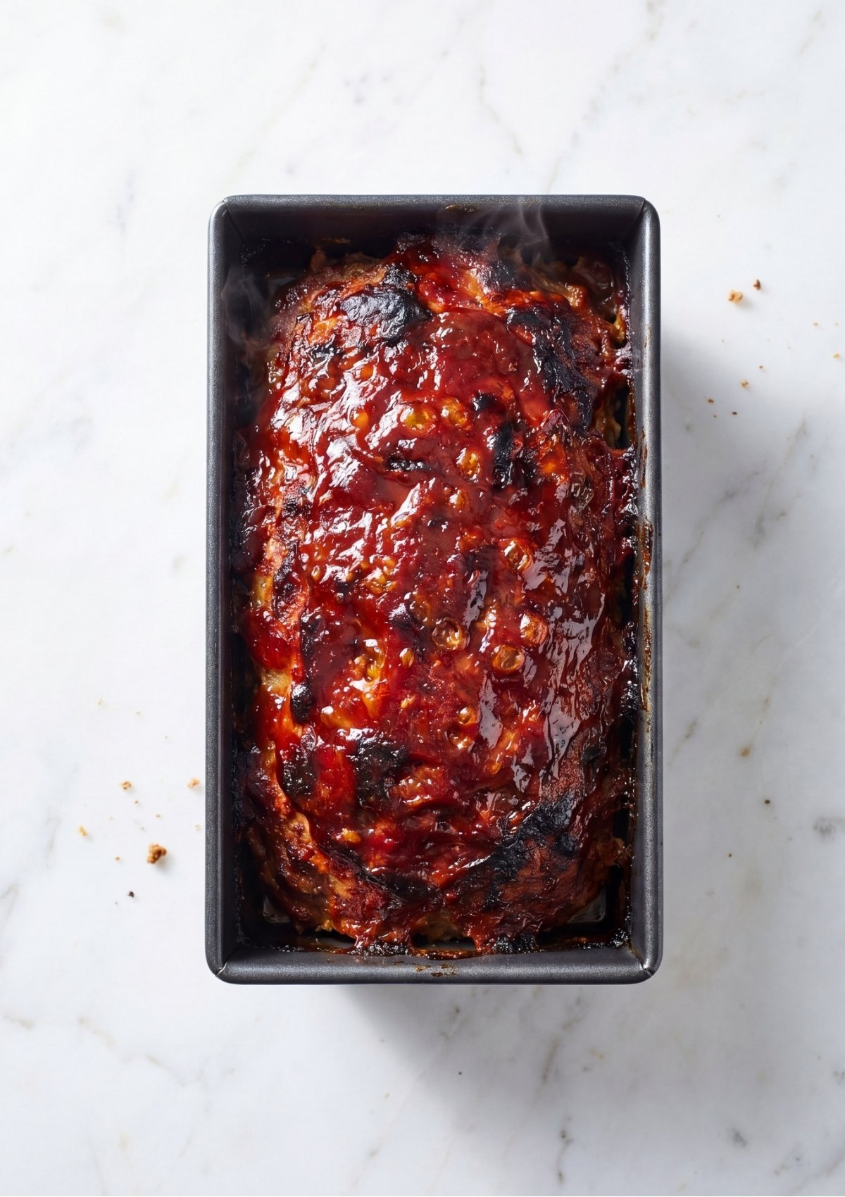 A fully baked turkey and beef meatloaf topped with a thick caramelized red glaze resting inside a metal loaf pan.