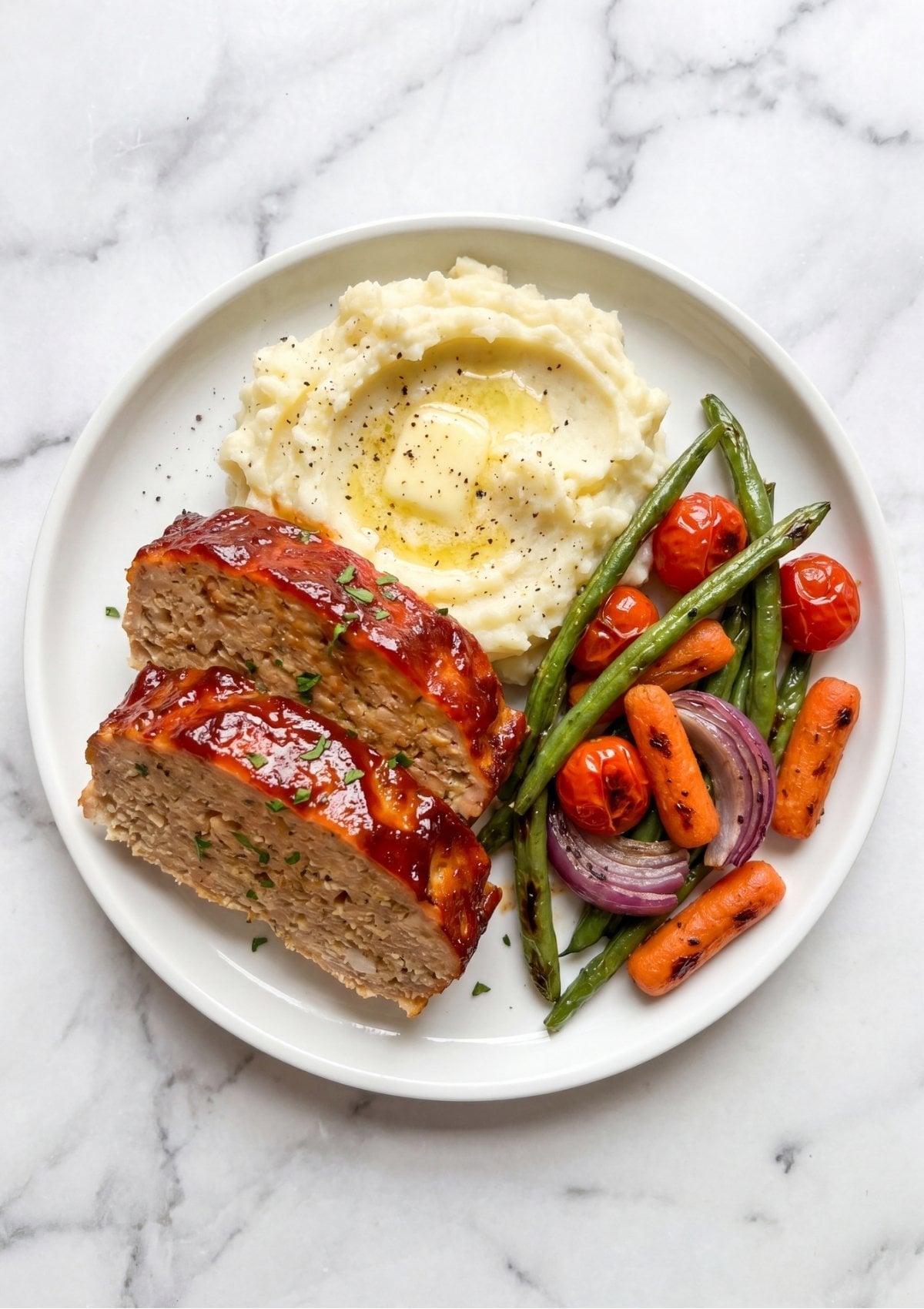 Two slices of glazed chicken meatloaf served with creamy mashed potatoes, green beans, and roasted carrots.