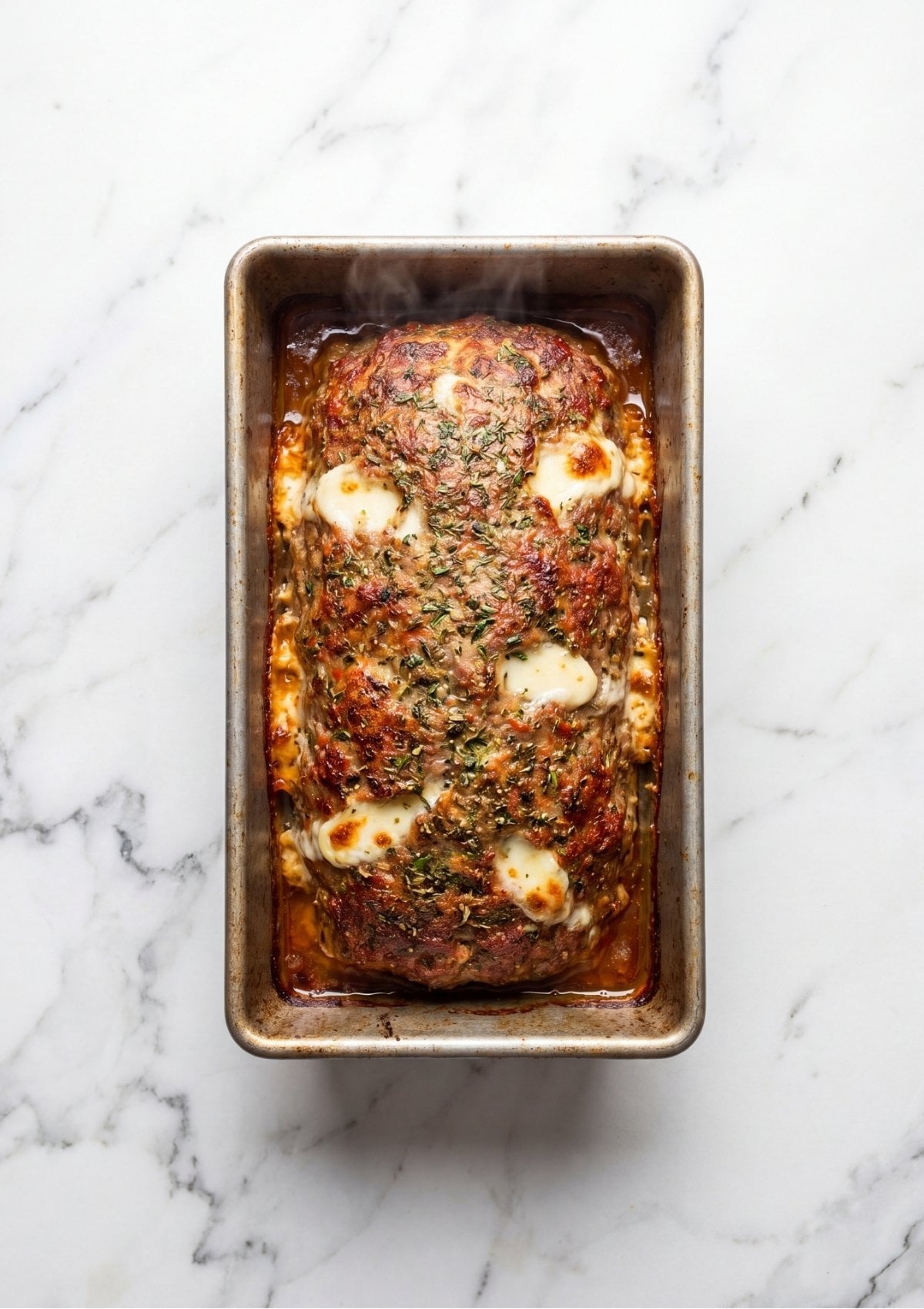 A fully cooked Italian meatloaf in a loaf pan with bubbling melted cheese and browned edges.