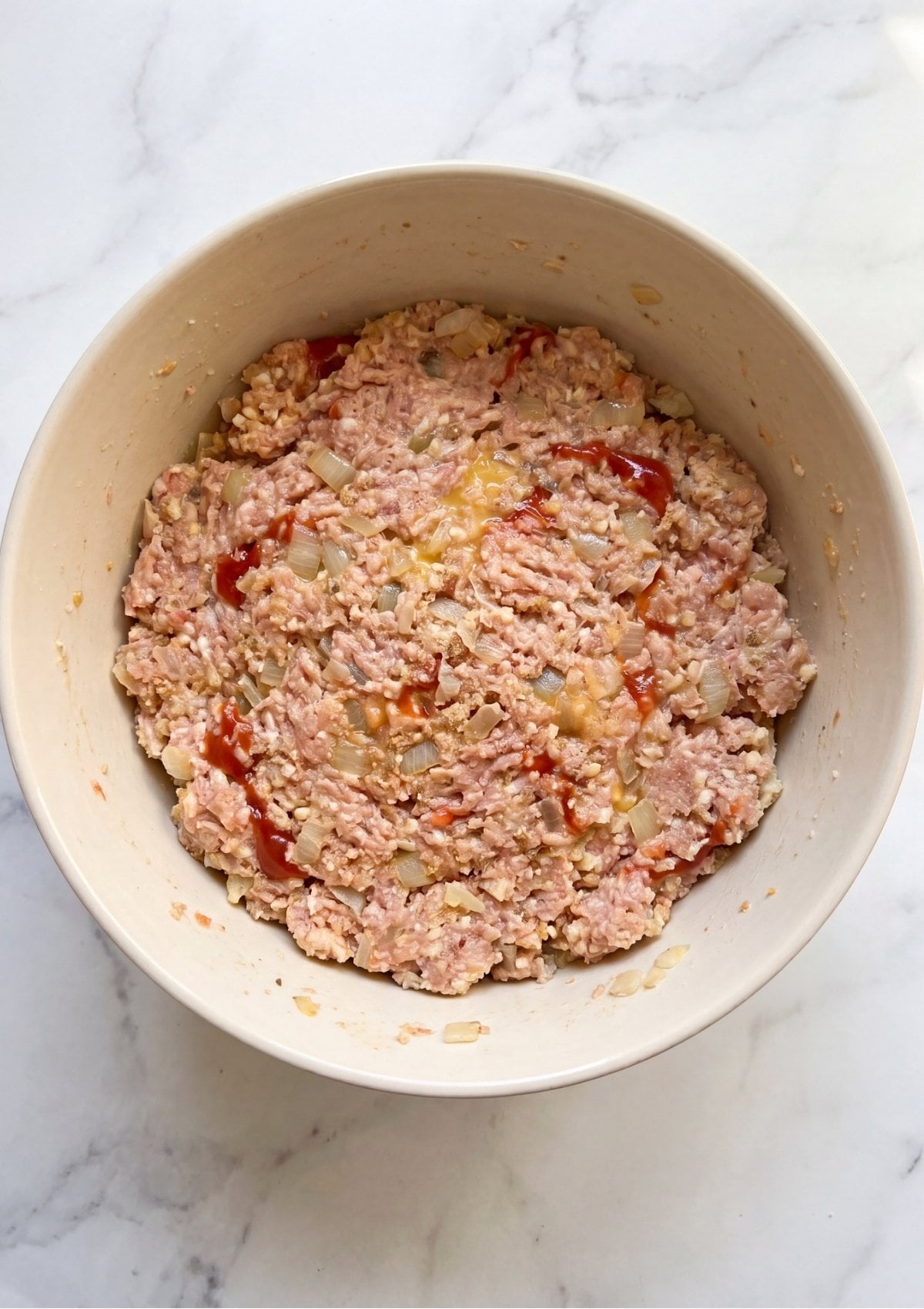 Raw ground turkey mixture with minced onions, egg, and ketchup being combined in a large white mixing bowl