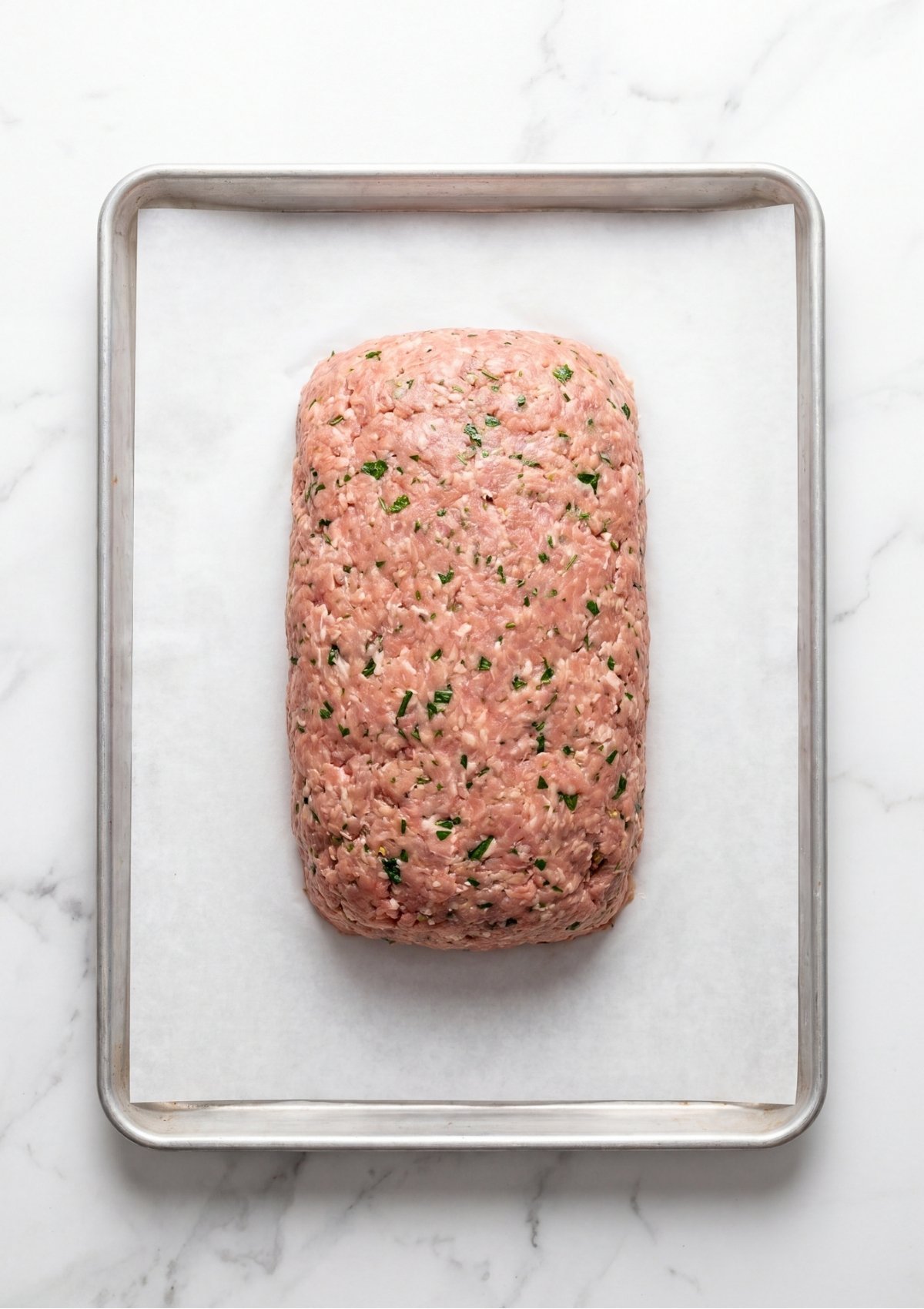 Raw seasoned ground turkey mixture shaped into a neat rectangular loaf on a parchment lined baking sheet.
